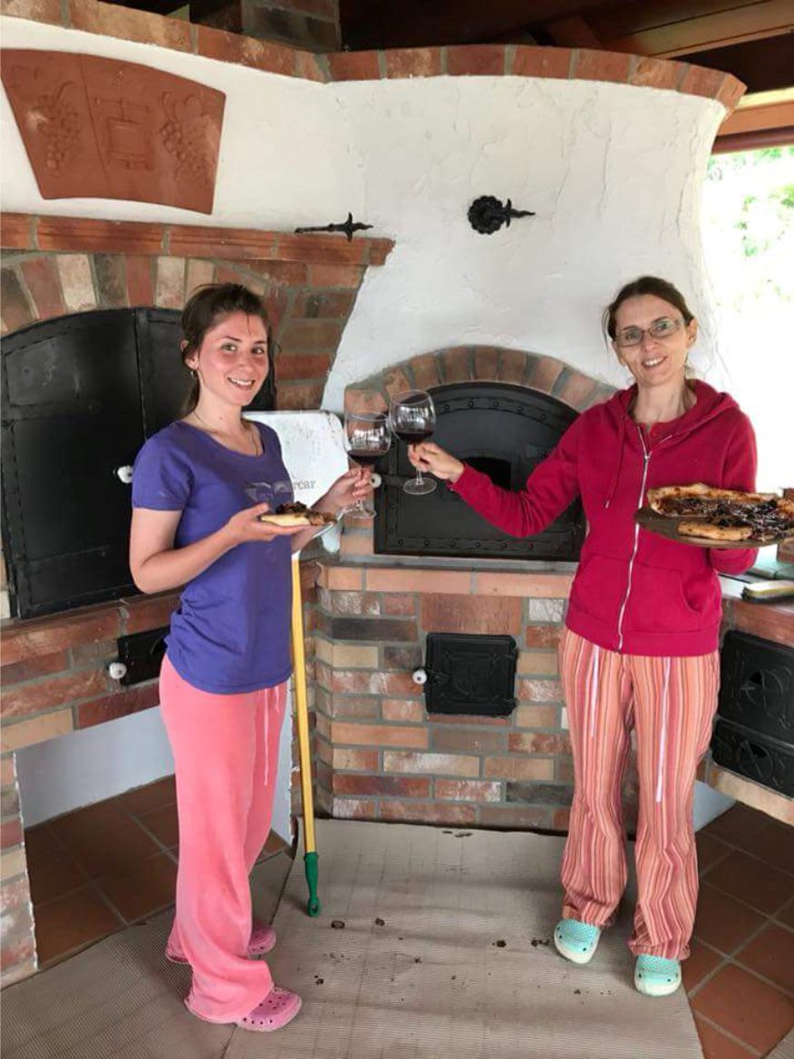 Dve ženy s pizzou a vínom pri peci na drevo v záhradnej kuchyni Pecmaniak